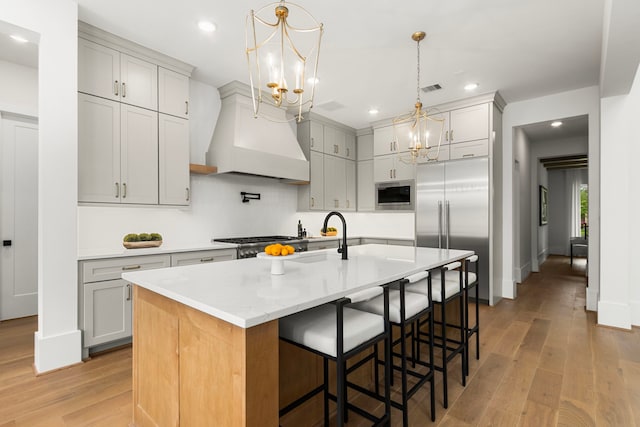 kitchen with built in appliances, an inviting chandelier, light wood-style flooring, visible vents, and a sink