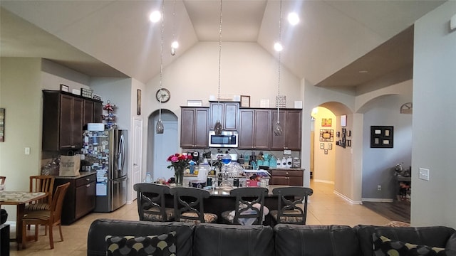 kitchen featuring high vaulted ceiling, backsplash, light tile patterned floors, dark brown cabinetry, and stainless steel appliances