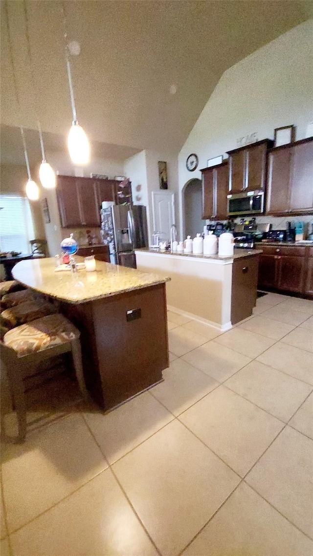 kitchen featuring a kitchen island, appliances with stainless steel finishes, decorative light fixtures, light tile patterned floors, and dark brown cabinetry