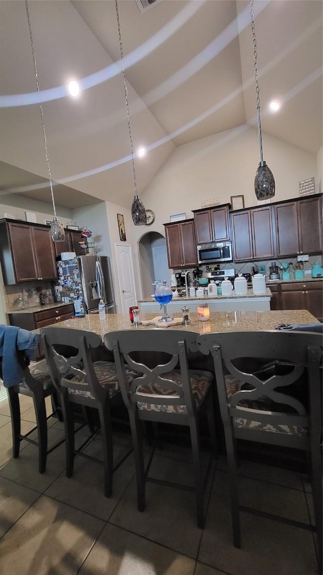 kitchen featuring stainless steel appliances, a large island, light stone counters, and a breakfast bar