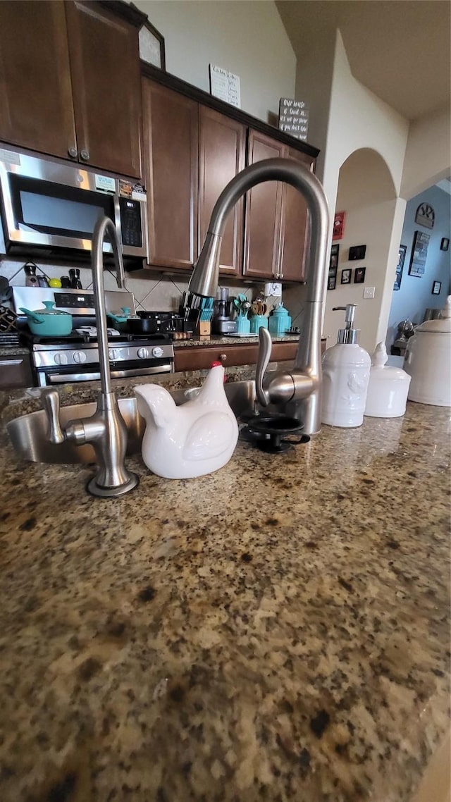 kitchen with dark brown cabinetry, stainless steel appliances, and dark stone counters