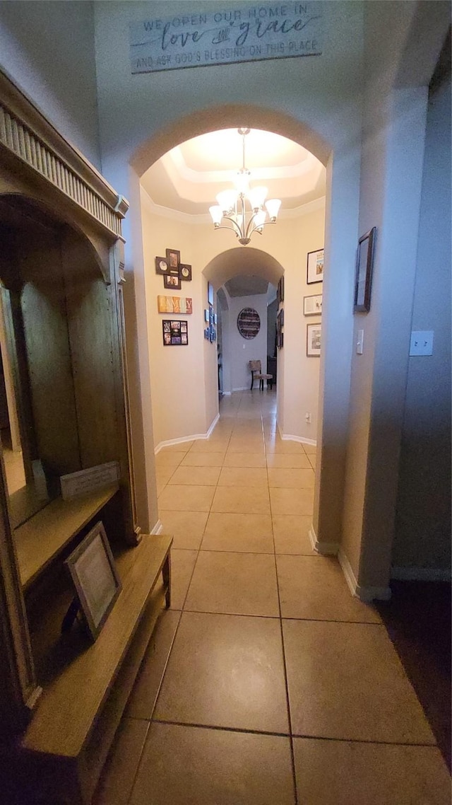 hall with tile patterned flooring, a raised ceiling, and a chandelier