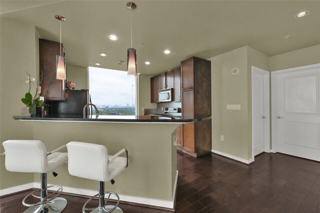 kitchen featuring hanging light fixtures, appliances with stainless steel finishes, kitchen peninsula, and dark hardwood / wood-style flooring