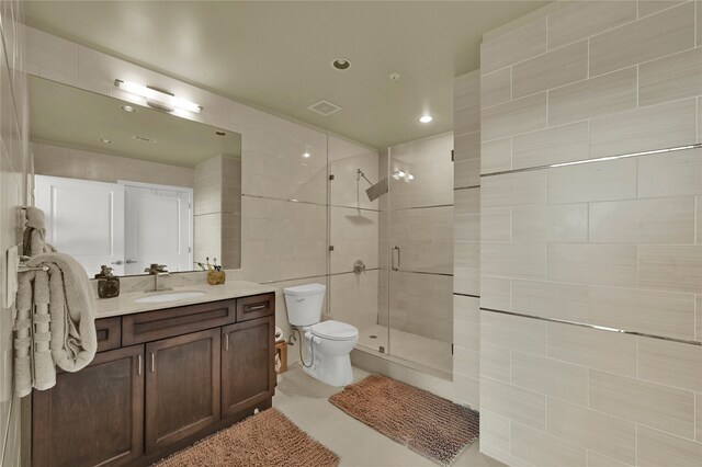 bathroom featuring a shower with shower door, toilet, tile walls, vanity, and tile patterned flooring