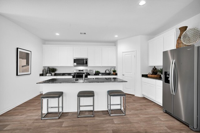 kitchen with appliances with stainless steel finishes, a kitchen island with sink, and white cabinets