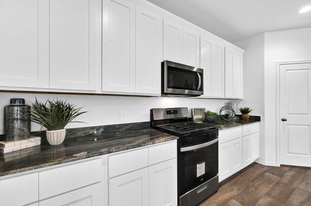 kitchen with stainless steel appliances, dark hardwood / wood-style flooring, dark stone counters, and white cabinets