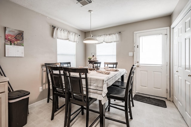 dining room featuring a textured ceiling, light floors, visible vents, and baseboards