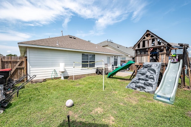 rear view of house with a shingled roof, a lawn, a playground, and fence