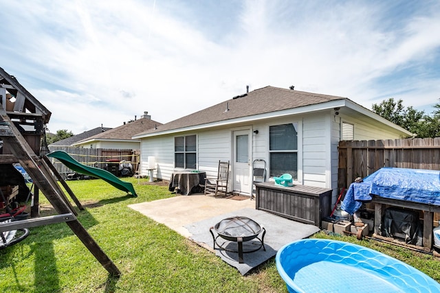 back of house featuring a playground, a fenced backyard, a fire pit, a yard, and a patio area