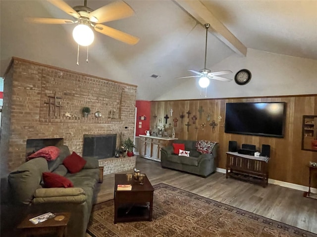 living room featuring wooden walls, vaulted ceiling with beams, hardwood / wood-style flooring, ceiling fan, and a brick fireplace