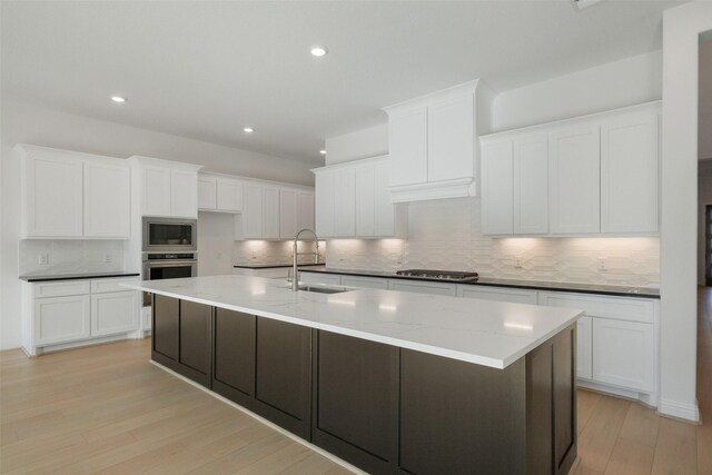 16006 Ruby Laurel Ct, Conroe, TX 77302 - kitchen with a sink, stainless steel appliances, decorative backsplash, light wood-type flooring, and a center island with sink