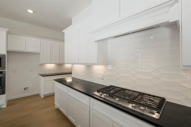 16006 Ruby Laurel Ct, Conroe, TX 77302 - kitchen featuring dark countertops, light wood finished floors, decorative backsplash, stainless steel appliances, and white cabinets