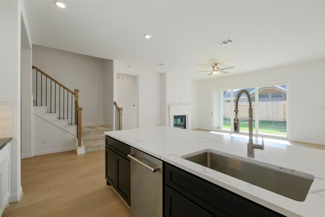 16006 Ruby Laurel Ct, Conroe, TX 77302 - kitchen featuring a sink, dishwasher, light wood finished floors, ceiling fan, and dark cabinets