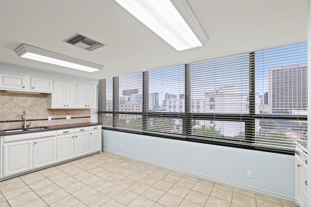 kitchen with light tile patterned floors, tasteful backsplash, white cabinetry, and sink