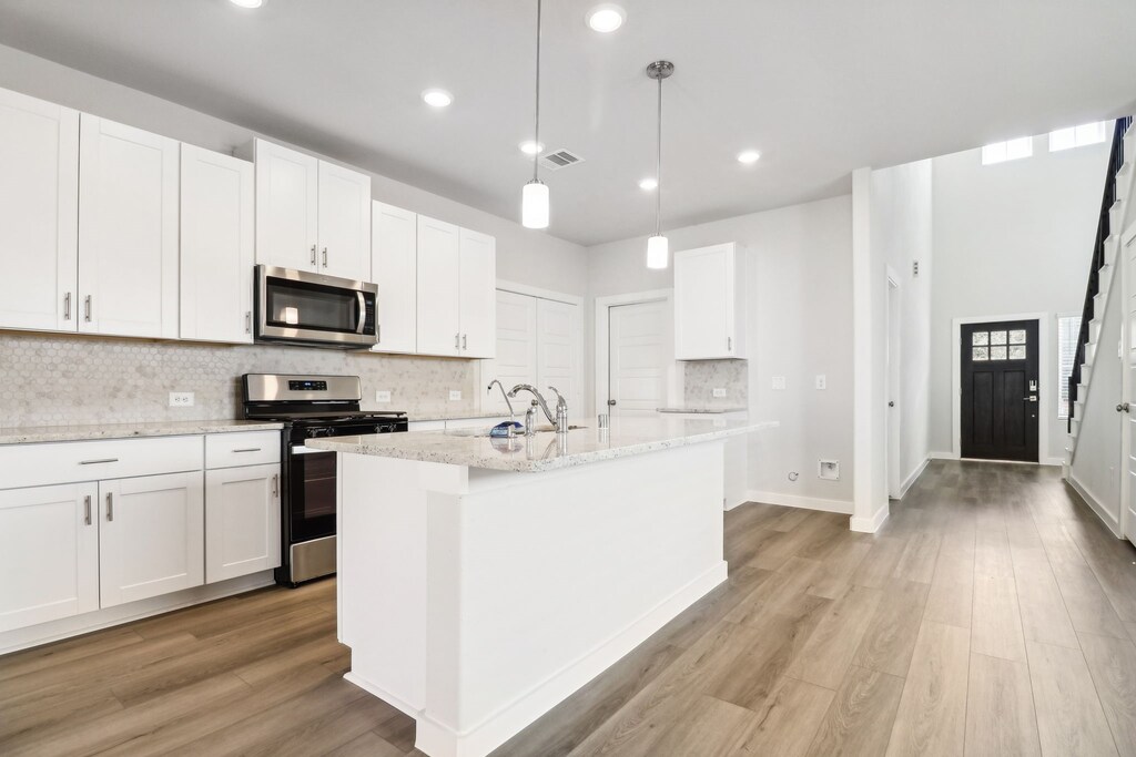 kitchen featuring decorative light fixtures, white cabinetry, a kitchen island with sink, and appliances with stainless steel finishes