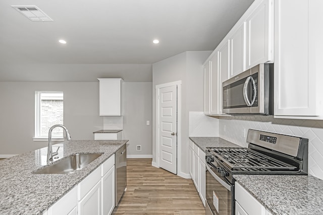 kitchen with backsplash, sink, light hardwood / wood-style floors, stainless steel appliances, and white cabinets