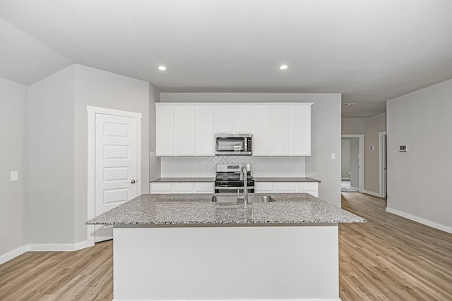 kitchen with white cabinets, light wood-type flooring, appliances with stainless steel finishes, and an island with sink