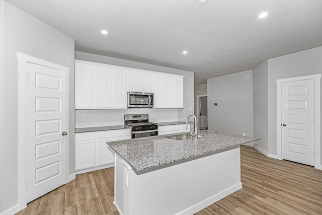 kitchen with light hardwood / wood-style floors, sink, stainless steel appliances, and a center island with sink