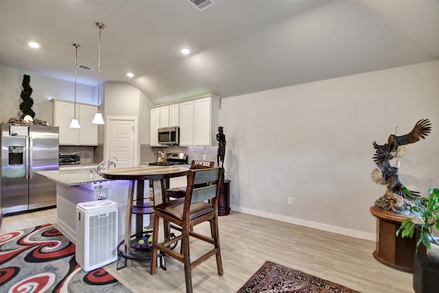 kitchen featuring tasteful backsplash, stainless steel appliances, a center island with sink, decorative light fixtures, and light stone countertops