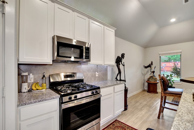 kitchen with light stone counters, lofted ceiling, stainless steel appliances, and white cabinets