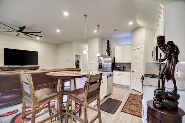 kitchen featuring appliances with stainless steel finishes, light stone counters, light hardwood / wood-style flooring, ceiling fan, and decorative light fixtures