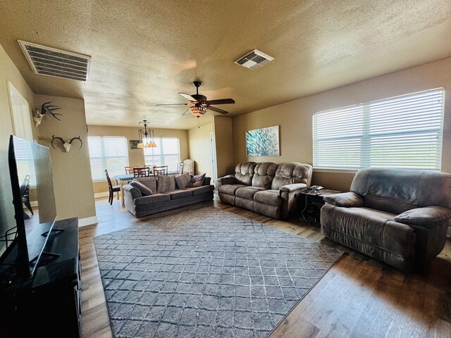 living room with hardwood / wood-style flooring, ceiling fan with notable chandelier, and a textured ceiling