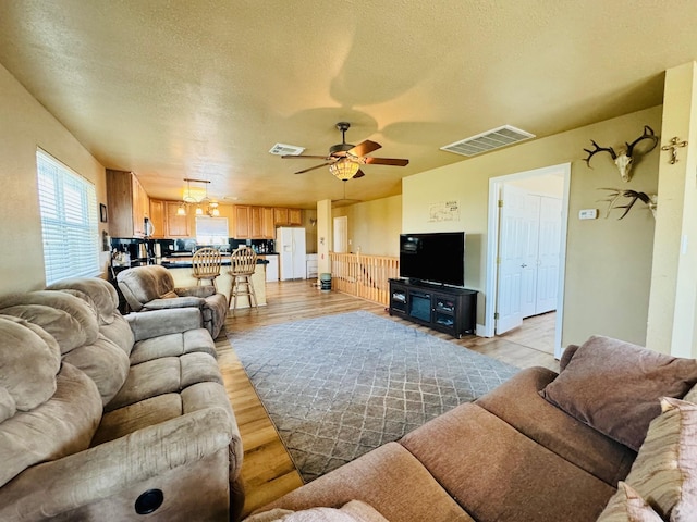 living room featuring a textured ceiling, ceiling fan, and light hardwood / wood-style floors