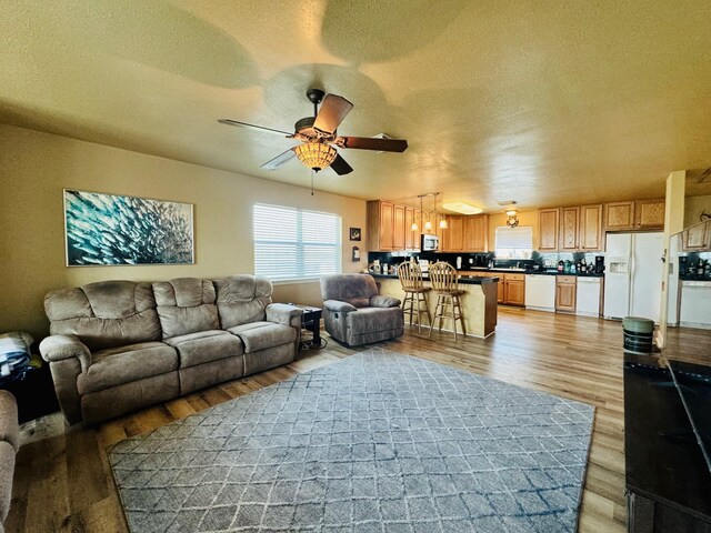 living room with ceiling fan, a textured ceiling, and light hardwood / wood-style flooring