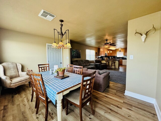 dining area featuring ceiling fan with notable chandelier and light hardwood / wood-style floors