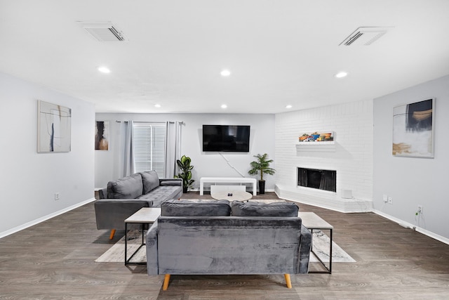 living room with dark hardwood / wood-style floors, brick wall, and a fireplace