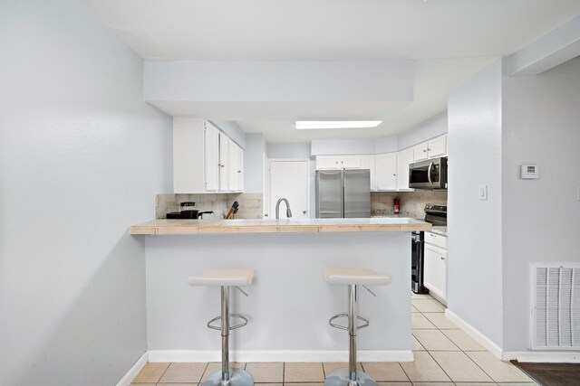 kitchen featuring stainless steel appliances, kitchen peninsula, decorative backsplash, and white cabinets