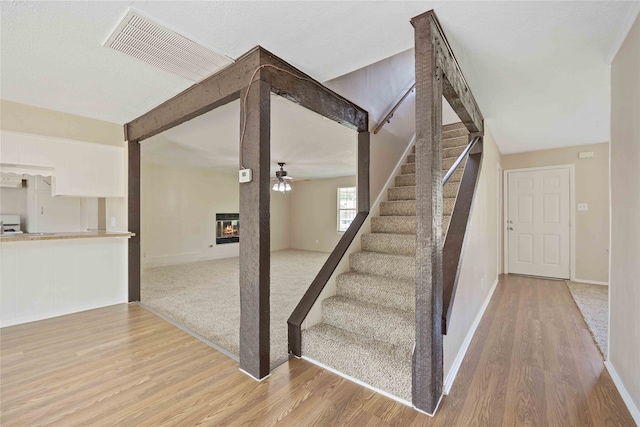 stairs featuring light hardwood / wood-style flooring, a fireplace, and ceiling fan