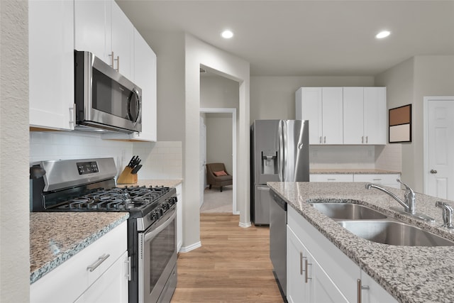 kitchen featuring light hardwood / wood-style flooring, tasteful backsplash, light stone countertops, appliances with stainless steel finishes, and sink