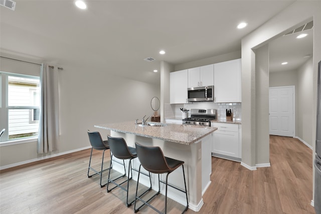 kitchen with appliances with stainless steel finishes, light hardwood / wood-style flooring, decorative backsplash, and light stone counters