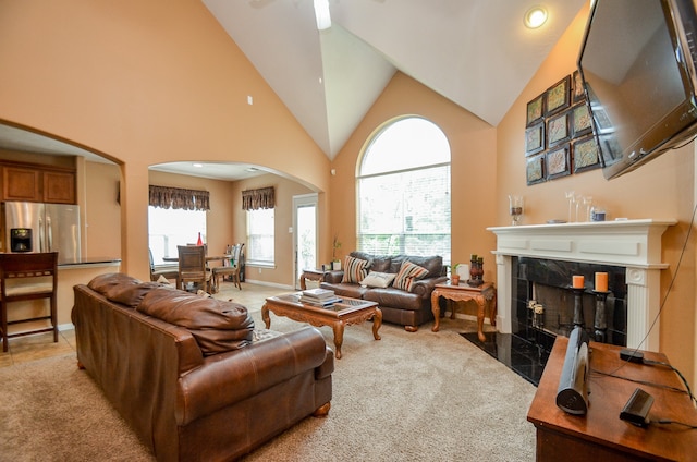 carpeted living room featuring a premium fireplace, high vaulted ceiling, and ceiling fan