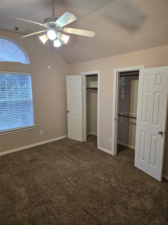 unfurnished bedroom featuring multiple closets, ceiling fan, a textured ceiling, lofted ceiling, and dark carpet