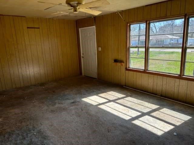 unfurnished room featuring plenty of natural light, wood walls, and ceiling fan