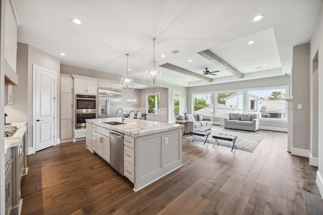 kitchen with sink, white cabinetry, an island with sink, stainless steel appliances, and beam ceiling