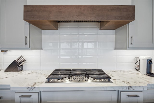 kitchen with tasteful backsplash, stainless steel gas stovetop, gray cabinets, and custom range hood