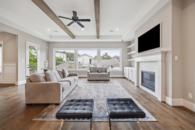 living room with hardwood / wood-style floors, beam ceiling, a tile fireplace, and ceiling fan