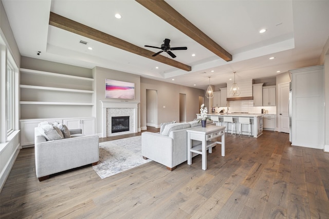 living room with beamed ceiling, ceiling fan, built in features, and light wood-type flooring