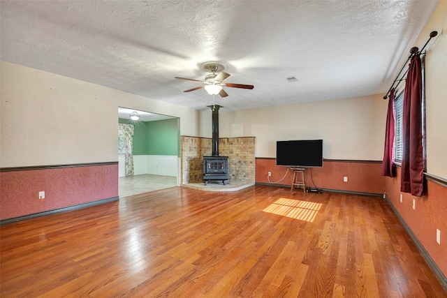 unfurnished living room with a wood stove, hardwood / wood-style floors, ceiling fan, and a textured ceiling