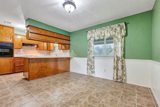 kitchen featuring a textured ceiling, kitchen peninsula, sink, decorative backsplash, and black oven