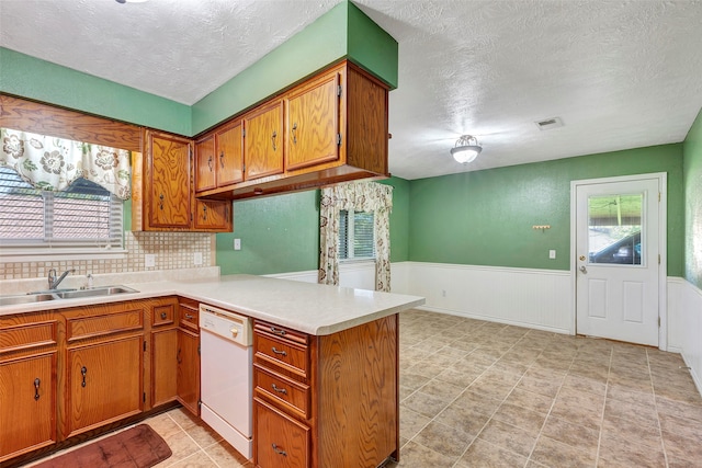 kitchen featuring white dishwasher, sink, kitchen peninsula, and a healthy amount of sunlight