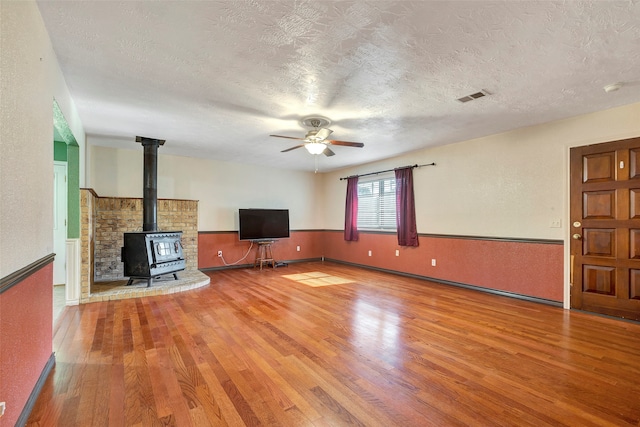 unfurnished living room with hardwood / wood-style floors, ceiling fan, a wood stove, and a textured ceiling