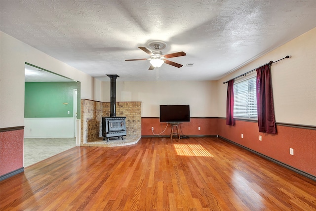 unfurnished living room with a wood stove, ceiling fan, hardwood / wood-style flooring, and a textured ceiling