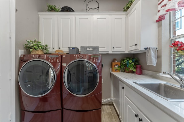 laundry room with sink, light hardwood / wood-style flooring, washing machine and dryer, and cabinets