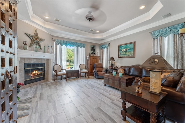 living room featuring ceiling fan, crown molding, a tray ceiling, and a tiled fireplace