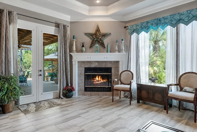 living area with a raised ceiling, french doors, a tiled fireplace, and a healthy amount of sunlight