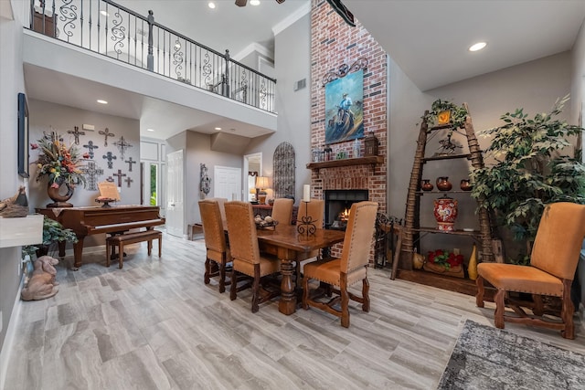 dining area featuring light hardwood / wood-style flooring, brick wall, a towering ceiling, and a brick fireplace